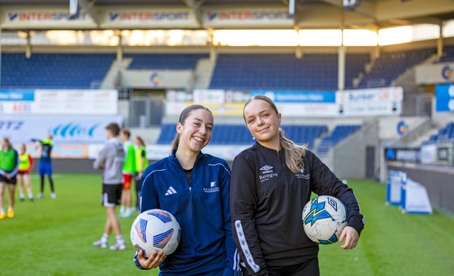 To jenter står på fotballbanen med hver sin fotball under armen.