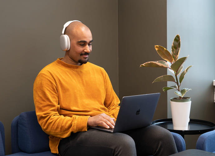 Privatist som jobber på Mac i sofa med headset. Foto.