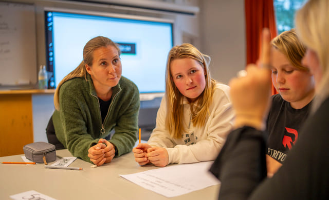 Lærer og elever i diskusjon i klasserommet.