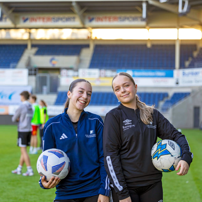 To elever på fotballbanen med hver sin fotball under armen.