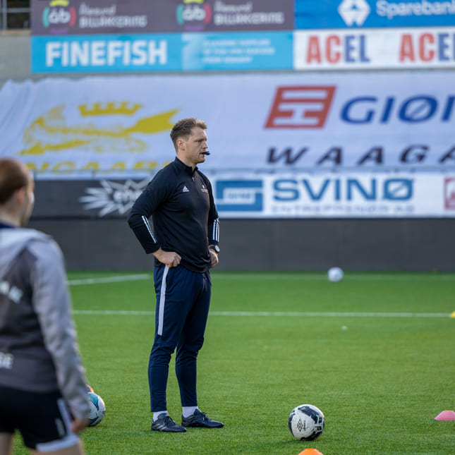 Akademietlærer står på fotballbanen og blåser i fløyta